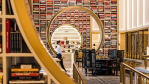 Una biblioteca con estanterías, un elemento decorativo circular y una persona caminando.