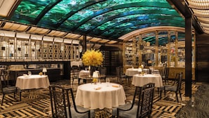 Un restaurante con mesas redondas, sillas y un techo con proyección de un árbol verde.