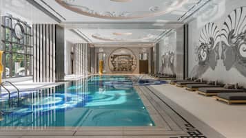 An indoor swimming pool with a modern design, including a geometric pattern on the floor, a central seating area with loungers, and a decorative wall mural.