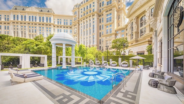 Un área de piscina de hotel lujosa, con una fuente central, tumbonas y un pabellón.