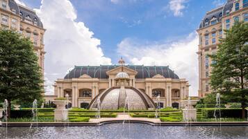Un edificio imponente con una cúpula central y una fuente, rodeado de jardines cuidados y árboles altos.