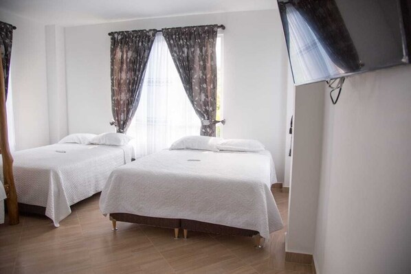 Una habitación con dos camas, piso de madera y cortinas en las ventanas.