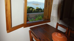 Un coin repas avec une table en bois, des chaises et une vue sur la mer par une fenêtre ouverte.