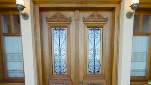 Une porte à deux battants en bois, ornée de panneaux de verre décoratifs et dotée d’une poignée en métal, flanquée de deux appliques murales.