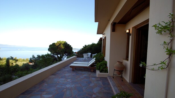 Un balcon avec un sol en pierre, deux fauteuils, une plante en pot et une vue sur la mer.