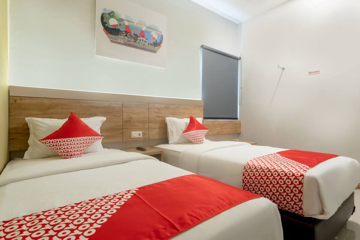 A hotel room with two beds, each with red and white bedding, a wooden headboard, a small bedside table, and a wall-mounted artwork.