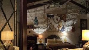 A rustic room with exposed wooden beams, a bed with a patterned blanket, a hanging light fixture, and a wall tapestry. - Unique Adobe Sanctuary w/hot tub close to hiking trails & wineries (San Marcos)