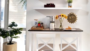 Una cocina con armarios blancos, una cafetera, una taza, una planta y un adorno en la pared.