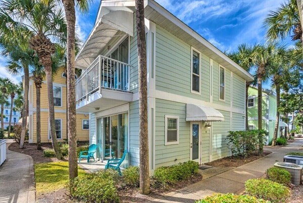 A two-story building with a balcony, surrounded by palm trees and a well-maintained lawn.