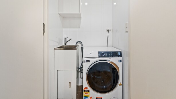 A compact laundry room with a washing machine and a small sink. - Iconic Views  (Kirribilli)