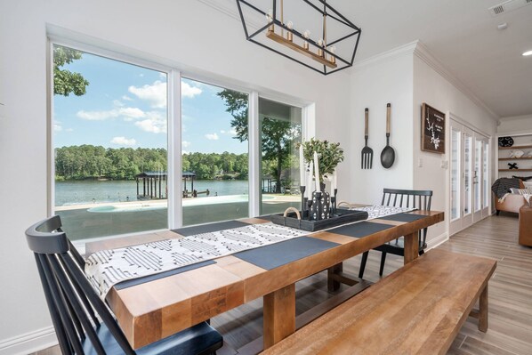 A dining area with a large wooden table, black chairs, and a view of a lake through large windows.