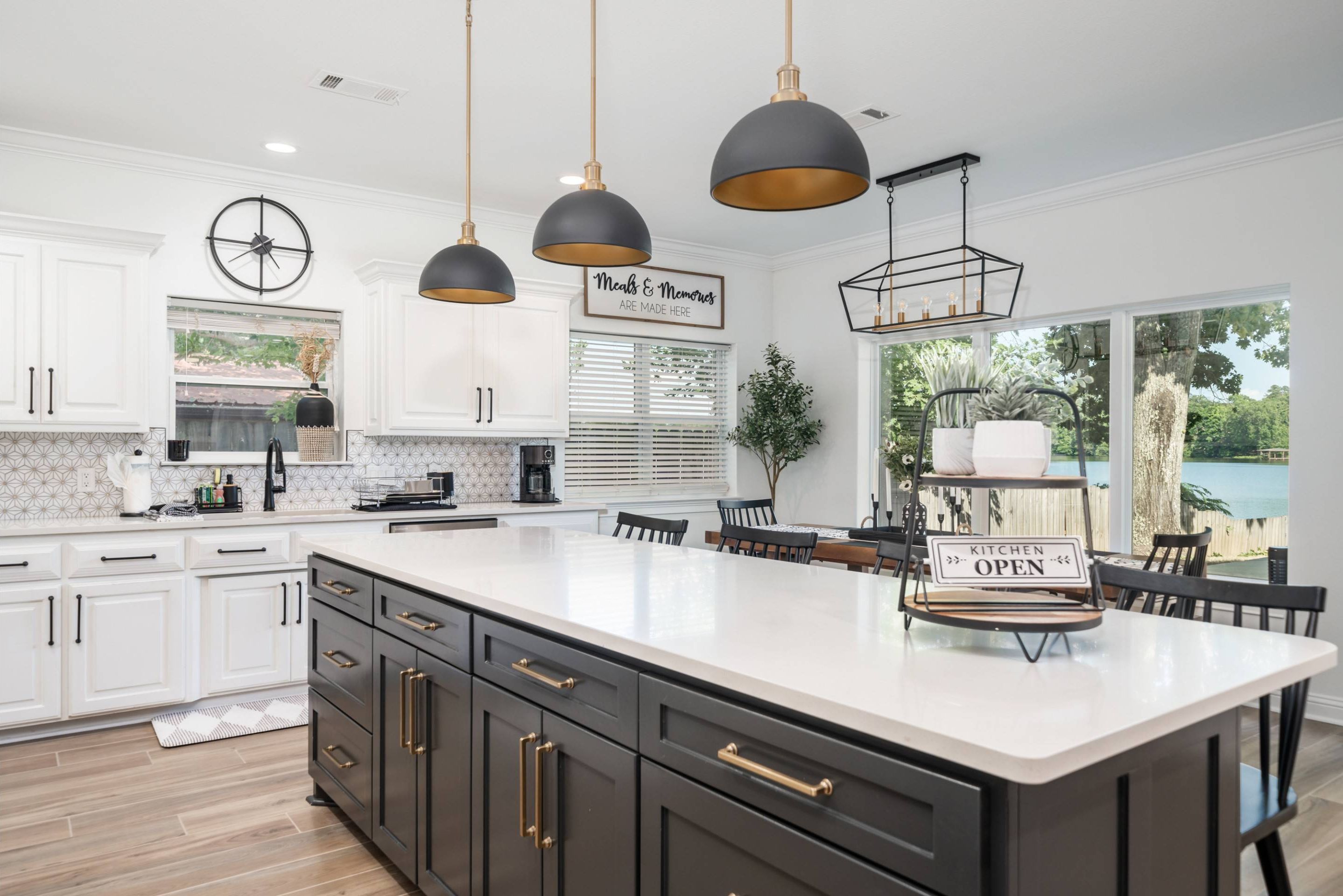 Een moderne keuken met witte kasten, een groot eiland, hanglampen en uitzicht op de omgeving.