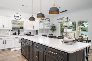 A modern kitchen with white cabinetry, a large island, pendant lighting, and a view of the outdoors.