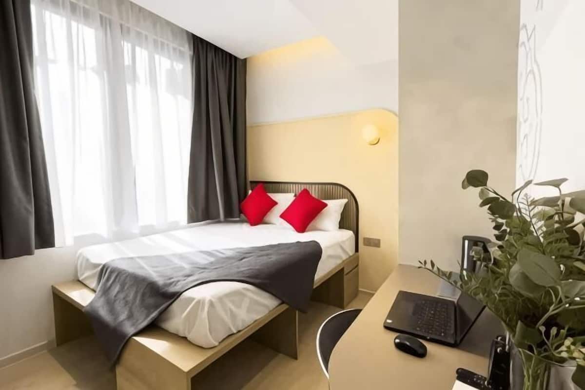 Une chambre d’hôtel avec un lit, un bureau, un ordinateur portable et une plante.
