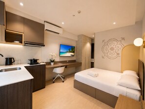 Una habitación de hotel moderna con kitchenette, una cama, un escritorio y un televisor.