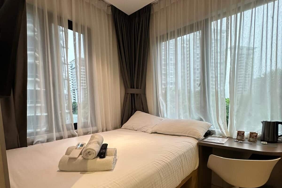 Une chambre d’hôtel avec un grand lit, un bureau avec une chaise et une fenêtre avec des rideaux.