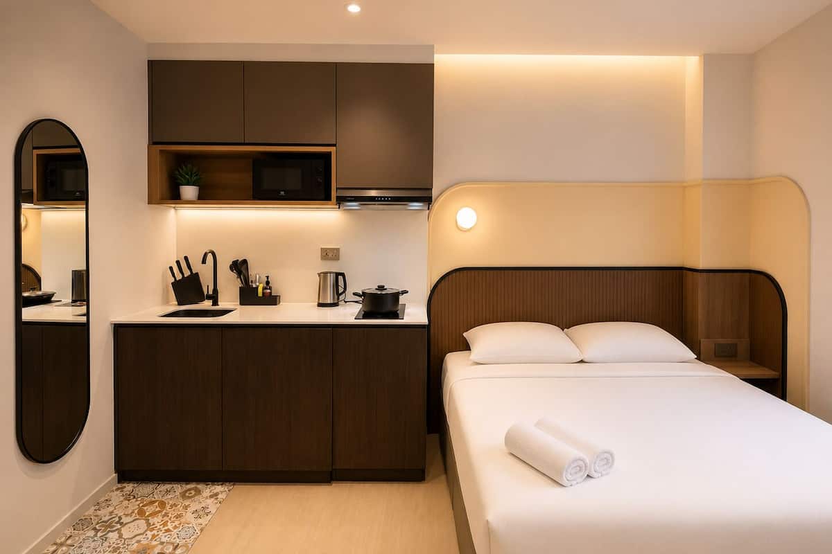 Une chambre d’hôtel avec une kitchenette, un lit avec du linge de lit blanc et une petite table de chevet.