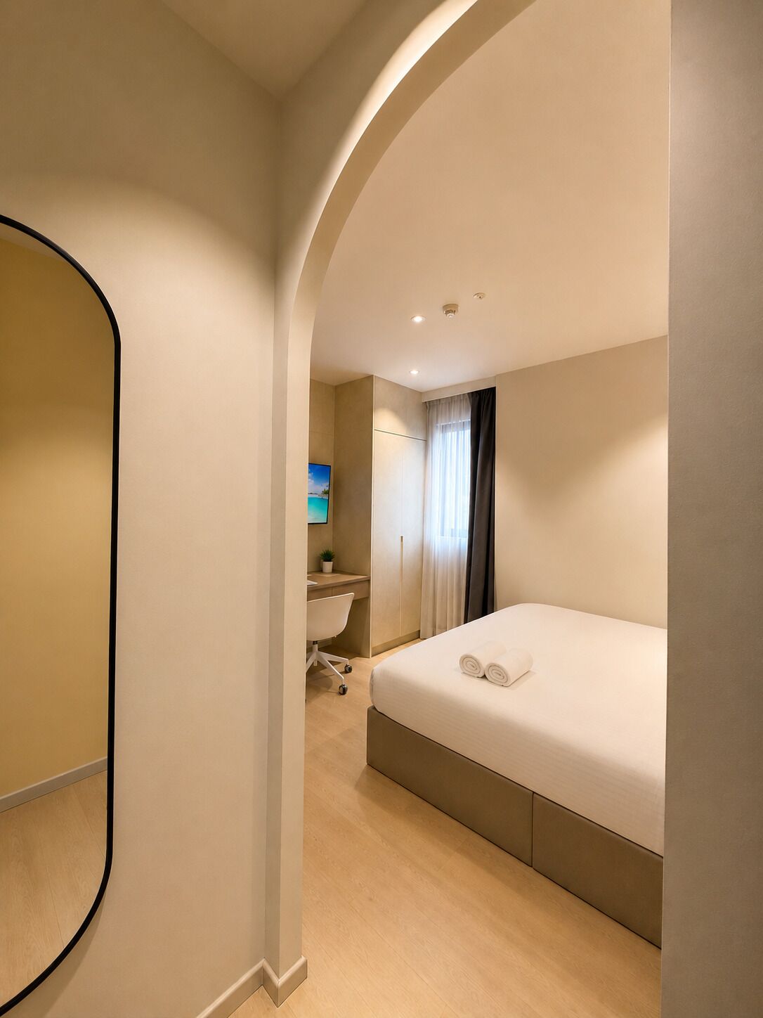 A modern hotel room with a curved wall, a bed, a desk, and a bathroom.