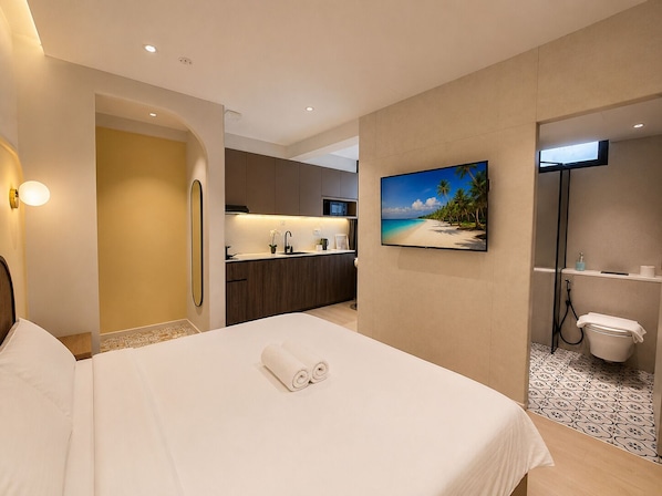 A hotel room with a bed, a bathroom, a kitchenette, and a TV on the wall.