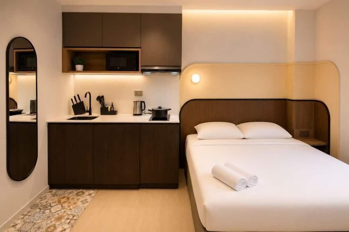 Une chambre d’hôtel avec un lit, une petite kitchenette, un miroir et une table de chevet.