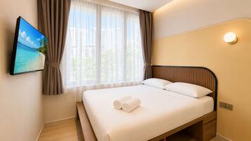 A hotel room with a bed, a TV mounted on the wall, and a window with curtains.