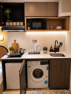 A compact kitchen with a microwave, kettle, sink, and a built-in washing machine.