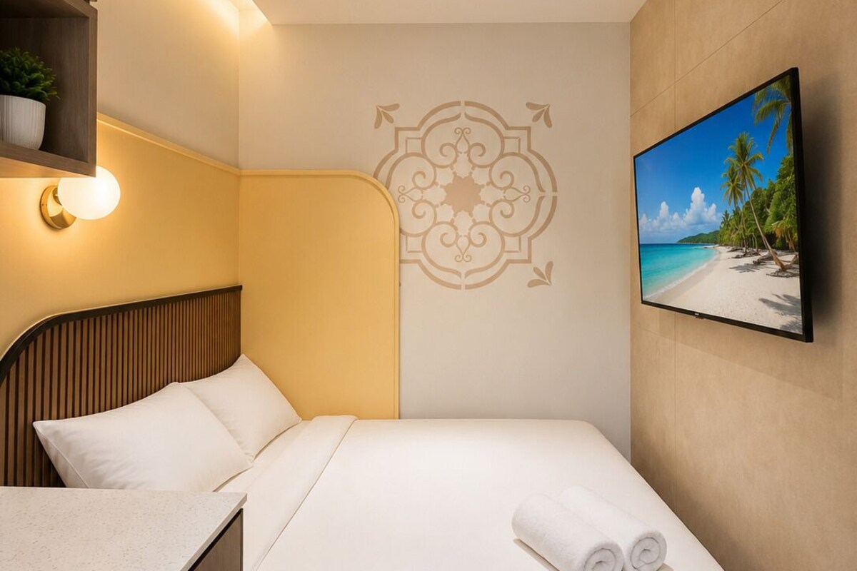 Habitació d'hotel amb un llit, televisió penjada a la paret, un disseny decoratiu a la paret i una petita estant amb una planta.