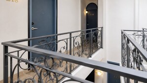 Un intérieur moderne avec une porte bleue, un escalier doté de rampes en fer forgé et un luminaire mural portant le numéro 218.