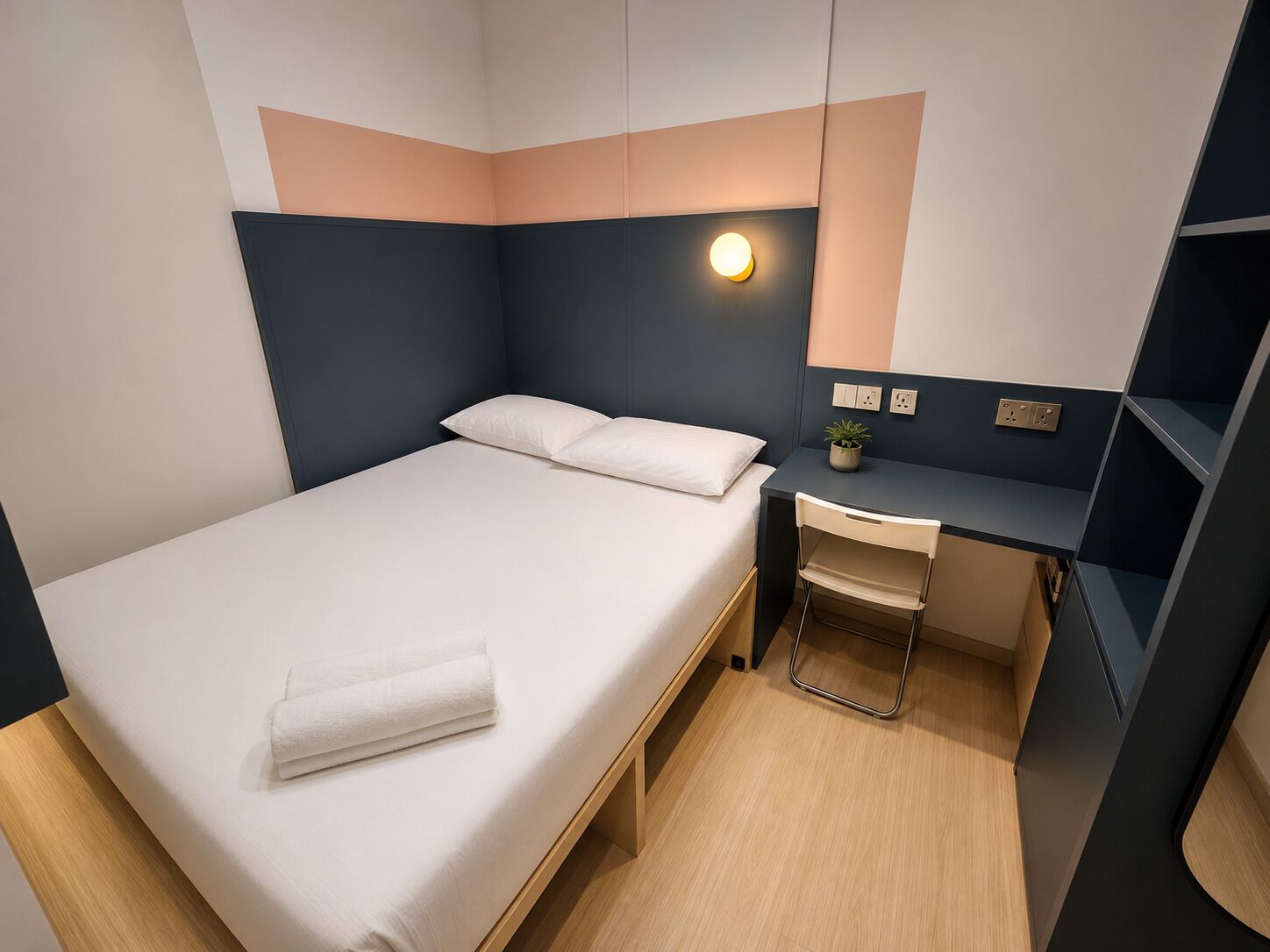 Une chambre à coucher moderne, comprenant un lit, une table de chevet, une chaise, un bureau et un luminaire fixé au mur.