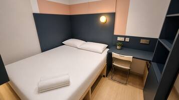 Une chambre à coucher moderne, comprenant un lit, une table de chevet, une chaise, un bureau et un luminaire fixé au mur.