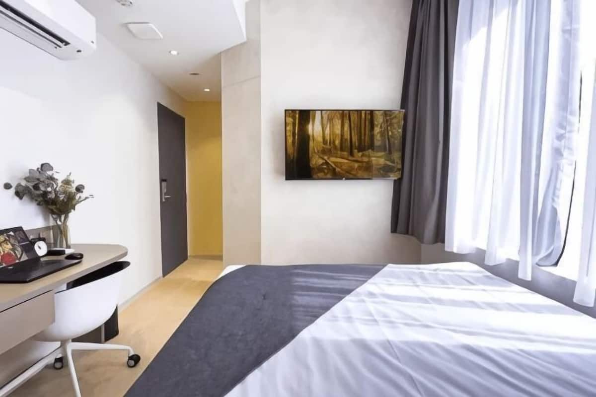 A modern hotel room with a bed, desk, and a painting on the wall.