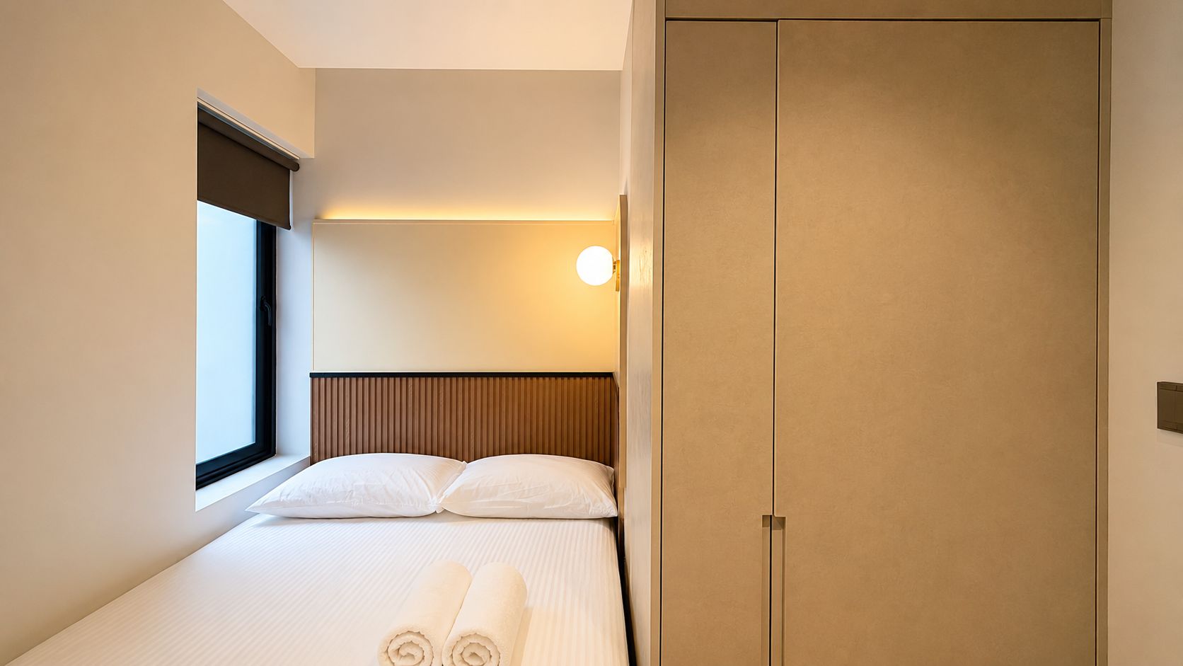 Habitación de hotel con una cama, ventana, lámpara en la pared y armario.