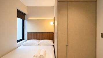 Habitación de hotel con una cama, ventana, lámpara en la pared y armario.