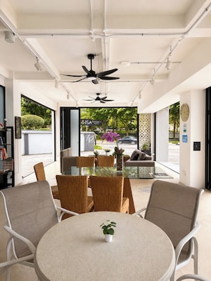 A modern hotel lobby with a round table, wicker chairs, ceiling fans, and a view of the ISA Academy Hotel.