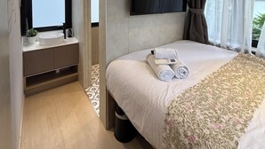 Une chambre d’hôtel moderne dotée d’un grand lit, d’un téléviseur à écran plat fixé au mur, d’une table de chevet avec un lavabo et d’une fenêtre avec des rideaux.