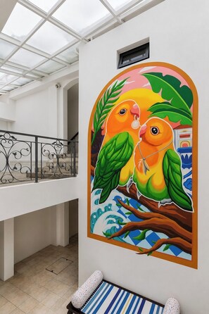 A mural of two birds on a branch, a white interior with a glass ceiling, and a patterned bench. - ISA Hotel Amber Road (Singapore)