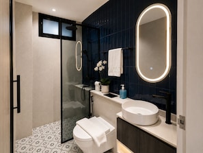 A modern bathroom with a glass-enclosed shower, a round sink, a large mirror, and a patterned floor.