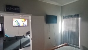 Un dormitorio con cama, televisor montado en la pared, ventana con cortinas y un letrero que dice 'SUNSHINE'.