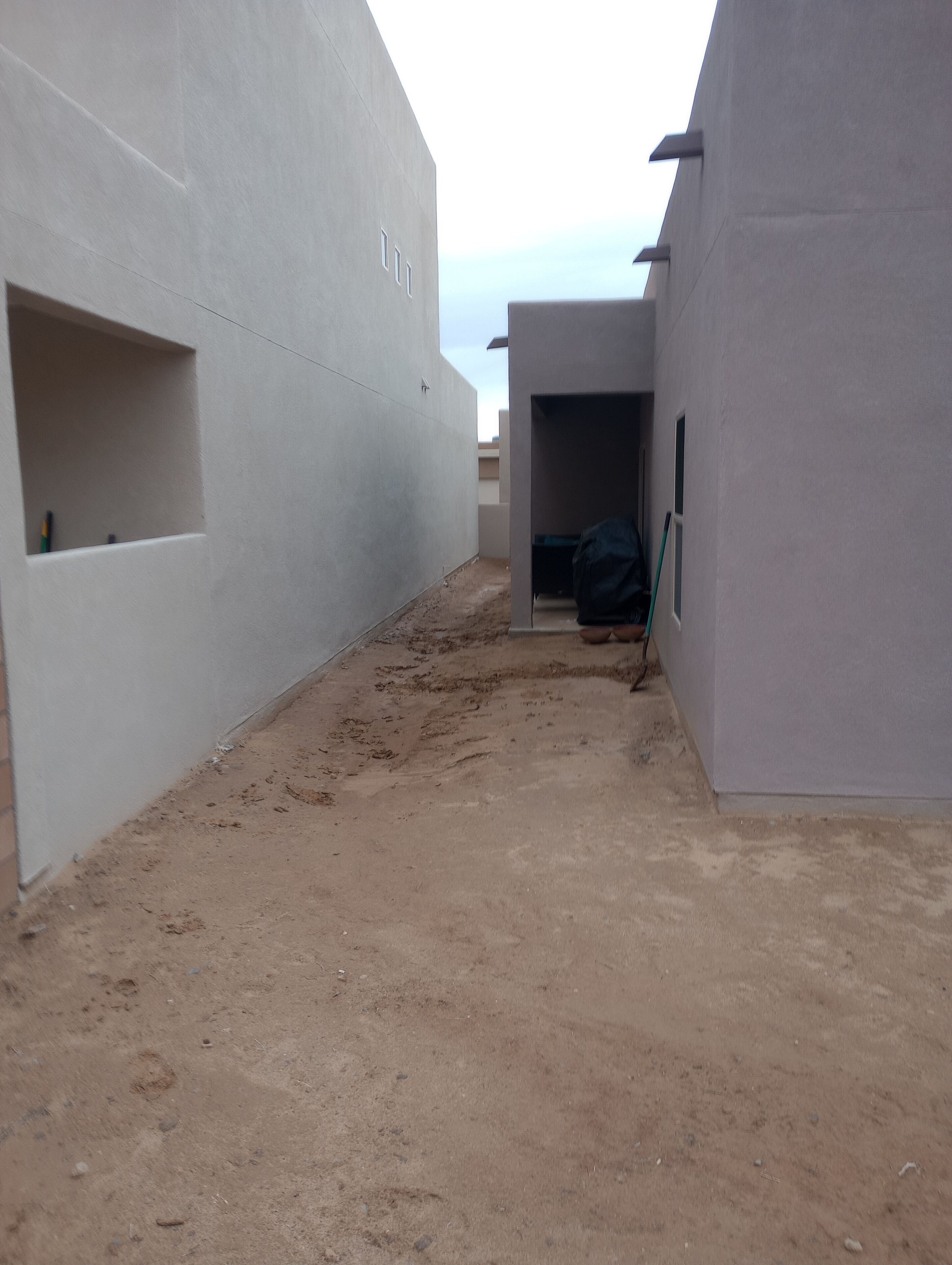 A narrow, sandy courtyard with white walls and a small window.