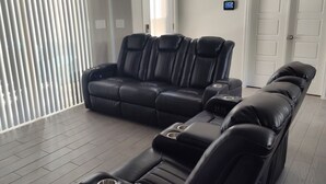 Una sala de estar moderna con un sofá seccional y un sillón reclinable, un ventilador de techo y un termostato en la pared.