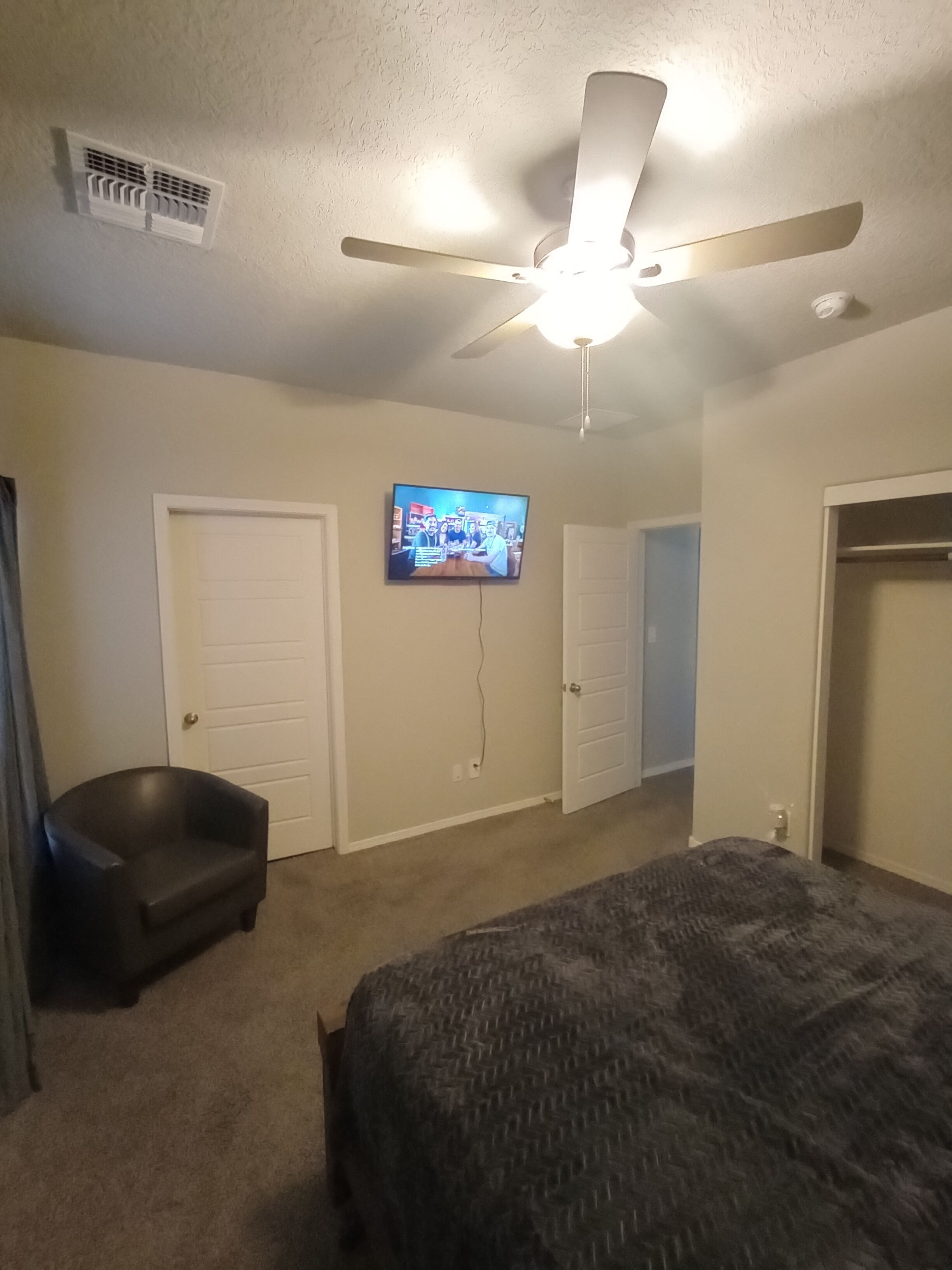 A bedroom with a bed, a ceiling fan, a TV, and two doors.