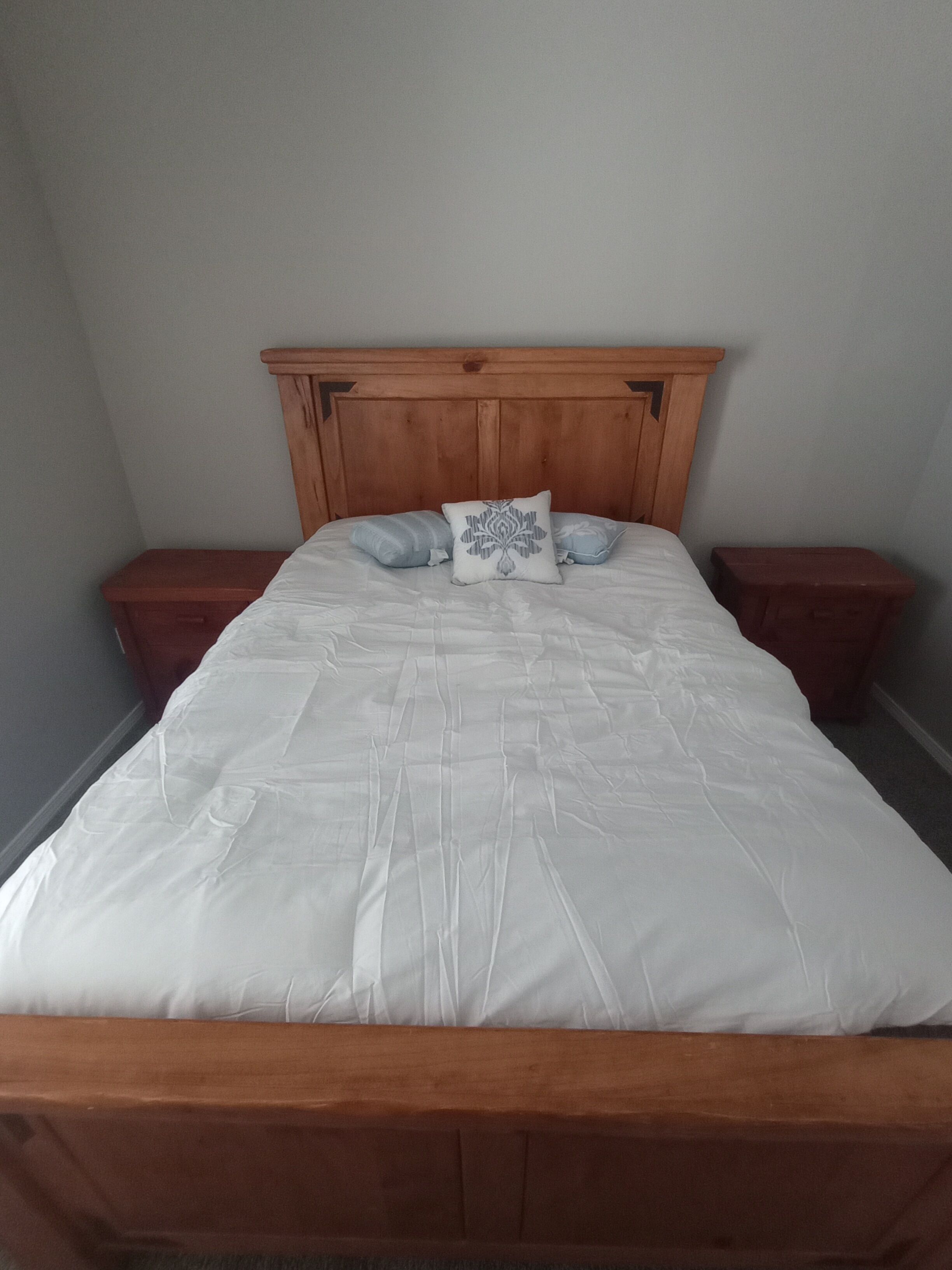 Ein Bett mit hölzernem Kopfteil, zwei Nachttische und einer weißen Bettdecke.