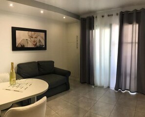 Una sala de estar moderna con un sofá oscuro, una mesa redonda con una botella y vasos, y un cuadro en la pared.