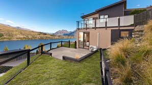 Una moderna casa a due piani con un balcone che si affaccia su un lago e montagne.