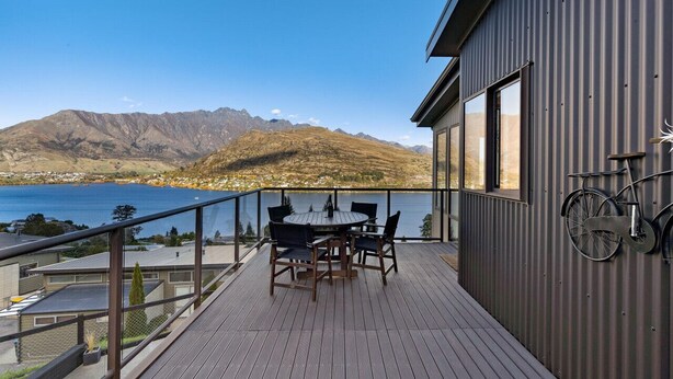 Una terrazza con tavolo e sedie che si affaccia su un lago e montagne.