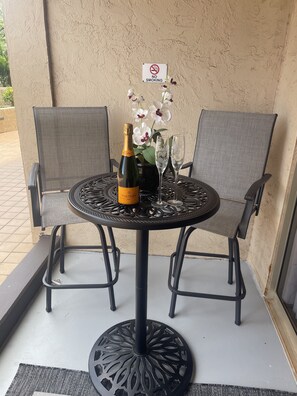 Ein runder Metalltisch mit zwei Stühlen, einer Champagnerflasche und zwei Gläsern auf einem Balkon mit einem Rauchverbot-Schild.