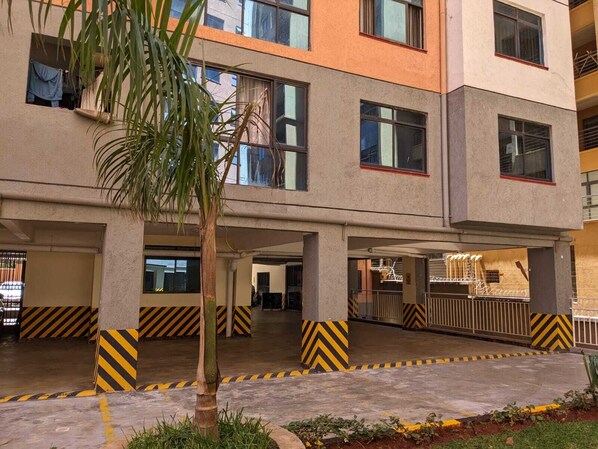 A multi-story building with a flat roof, large windows, and a parking area with yellow and black striped barriers.