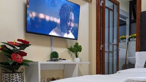 Une chambre d’hôtel avec un lit, un téléviseur fixé au mur, un petit bureau blanc et une plante en pot.