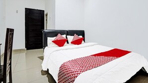 Un lit bien fait, recouvert d’une couvre-lit à motifs rouges et blancs, avec deux oreillers aux motifs rouges et blancs, et une tête de lit noire.