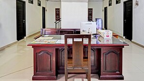 Un comptoir d’accueil avec un ordinateur, des papiers et une chaise, situé dans un couloir dont le sol est carrelé et les portes sont noires.